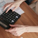 Close-up of a woman using a calculator and reviewing bills at home.